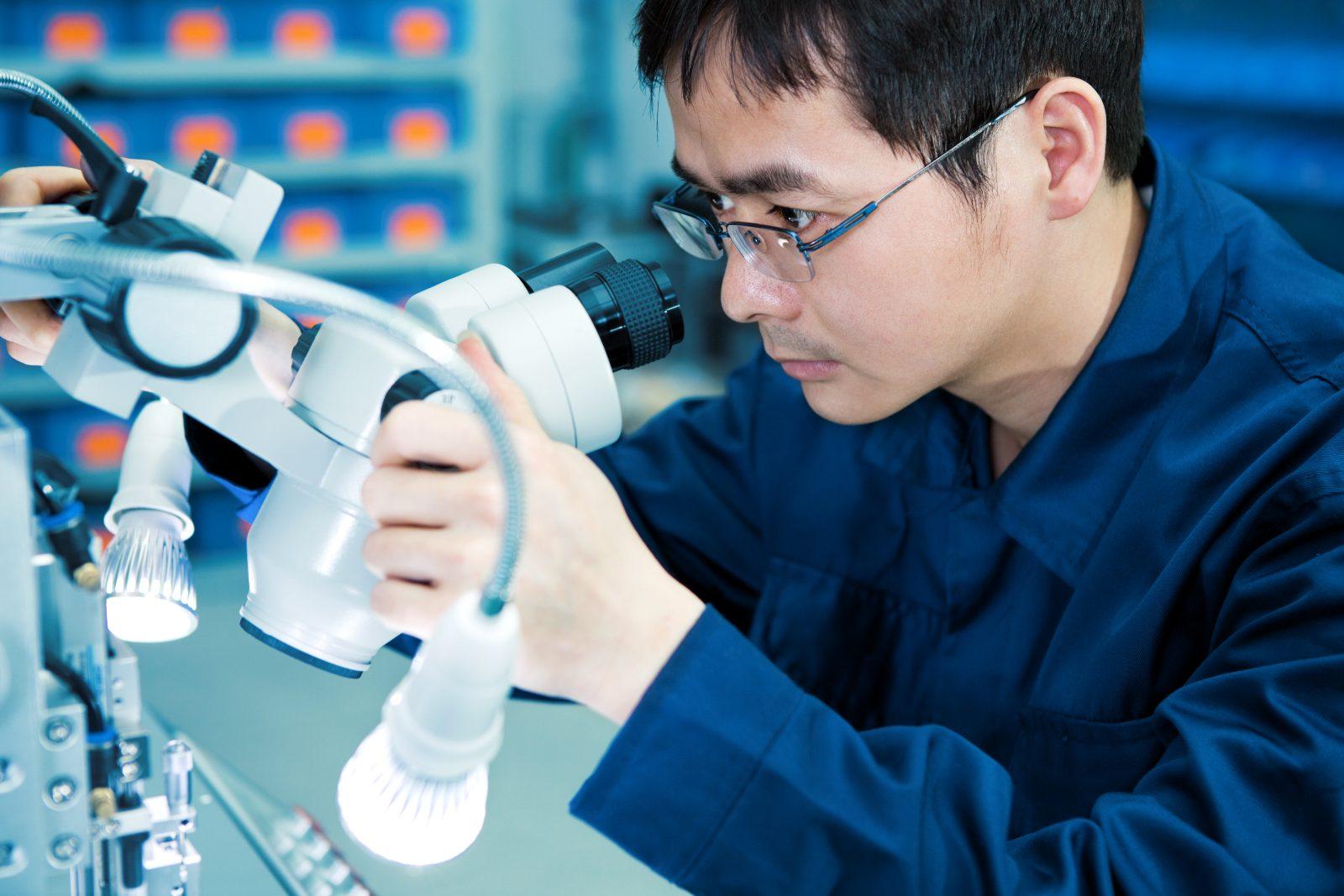 A technician inspecting electronics through a microscope in the lab